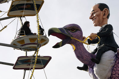 A large carnival float depicting Italian Prime Minister Silvio Berlusconi riding a giant bird passes by a Ferris wheel during a carnival parade in Viareggio, northern Italy, February 19, 2006. The carnival is characterised by its political and religious satire. 