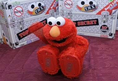 A new T.M.X. ELMO, making its global debut on the tenth anniversary of Tickle Me Elmo, slaps his knee on a table at KB Toys at Manhattan Mall in New York, Tuesday, Sept. 19, 2006. He's still red, fuzzy and really ticklish, but now Elmo's laughing fits have him , falling to the floor, slapping his knee, rolling over and pounding his arm. Fisher-Price, a unit of Mattel Inc., on Tuesday took the wraps off T.M.X. Elmo, ending months of unprecedented secrecy that's had the toy industry abuzz.