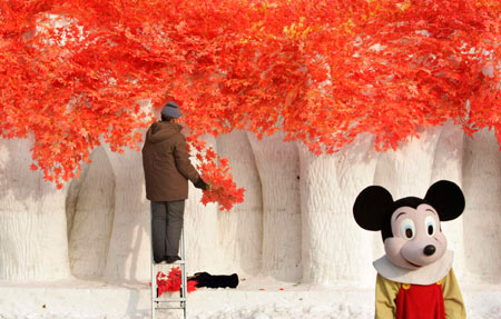 An elderly man prepares a snow sculpture for the upcoming the China Harbin international ice and snow festival as a girl dressed as Mickey Mouse poses at a park in Harbin, northeastern China's Heilongjiang Province, January 4, 2007.