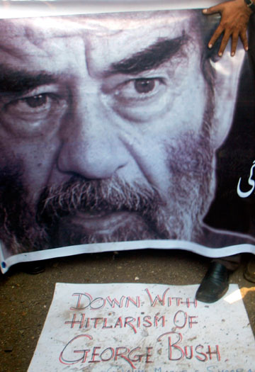 A protester holds a banner with a picture of executed former Iraqi president Saddam Hussein as he steps on an anti-U.S. placard in Mumbai December 30, 2006.